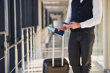 Close up view of male passenger in elegant formal clothes that is in the airport hall with baggage and tickets.