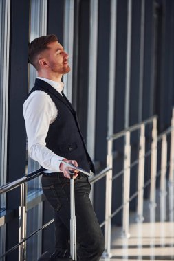 Şık giyinmiş genç bir erkek yolcu havaalanı salonunda bavullarıyla bekliyor..