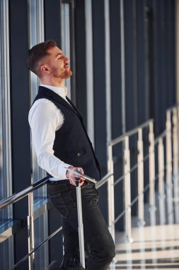 Şık giyinmiş genç bir erkek yolcu havaalanı salonunda bavullarıyla bekliyor..