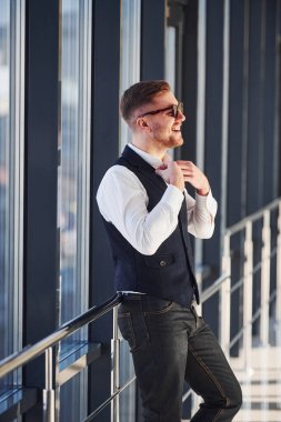 Zarif elbiseli ve güneş gözlüklü bir adam içeride kameraya poz veriyor..