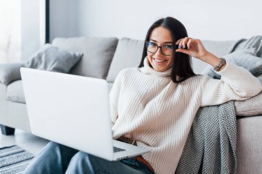 Gözlüklü genç bir kadın evde dizüstü bilgisayarla oturuyor..