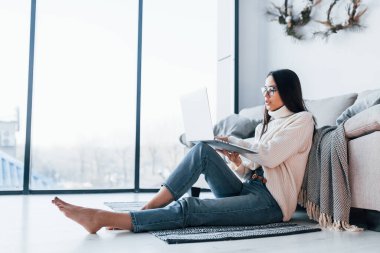 Young beautiful woman in glasses sitting at home alone with laptop.