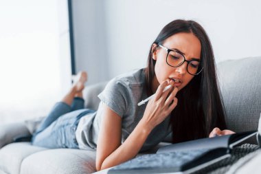 Gündelik giysiler içinde genç ve güzel bir kadın not defteri ve kalemle evde tek başına yatıyor..