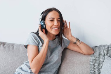 Gündelik giysiler içinde, evde tek başına oturmuş kulaklıkla müzik dinleyen güzel bir kadın..