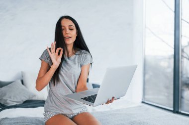 Bilgisayarı kullanarak çevrimiçi konuşma. Gündelik giysiler içinde evde yalnız oturan genç ve güzel bir kadın..