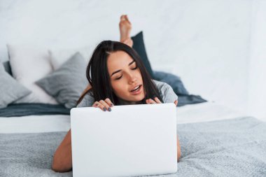 Young beautiful woman in casual clothes lying down at home alone with laptop.