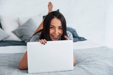 Young beautiful woman in casual clothes lying down at home alone with laptop.