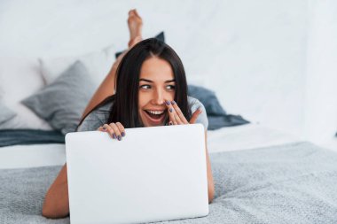 Young beautiful woman in casual clothes lying down at home alone with laptop.