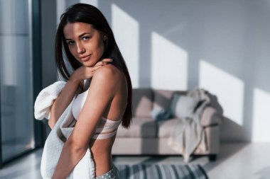 Genç, güzel esmer kız, içeride duruyor ve vücudunu beyaz havluyla örtüyor..