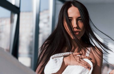 Genç, güzel esmer kız, içeride duruyor ve vücudunu beyaz havluyla örtüyor..