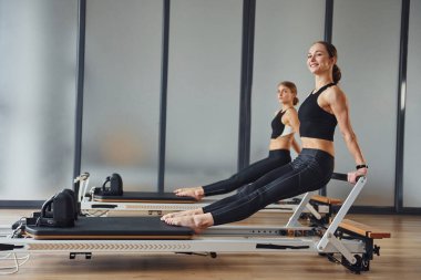 Eller güçlü. Spor elbiseli ve zayıf vücutlu iki kadın kapalı alanda spor yoga yapıyorlar..