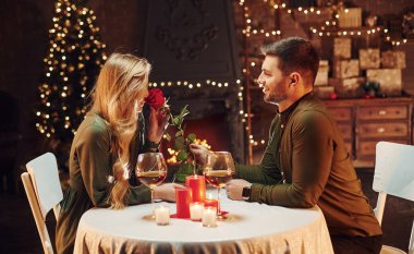 Güzel kırmızı bir gül tutuyordu. Genç ve güzel çift evde romantik bir akşam yemeği yiyor..