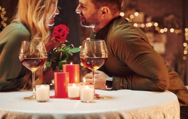 Güzel kırmızı bir gül tutuyordu. Genç ve güzel çift evde romantik bir akşam yemeği yiyor..