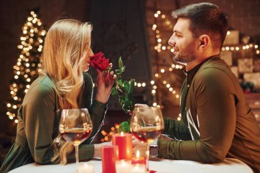 Güzel kırmızı bir gül tutuyordu. Genç ve güzel çift evde romantik bir akşam yemeği yiyor..