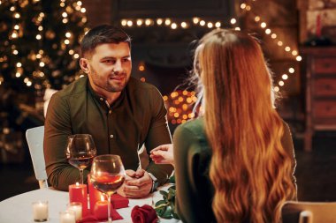 Masanın yanında oturuyor. Genç ve güzel çift evde romantik bir akşam yemeği yiyor..