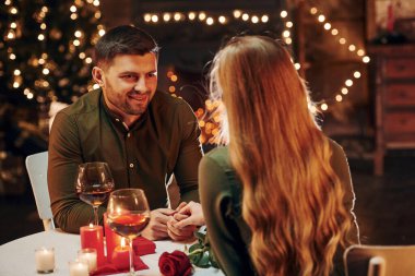 Masanın yanında oturuyor. Genç ve güzel çift evde romantik bir akşam yemeği yiyor..