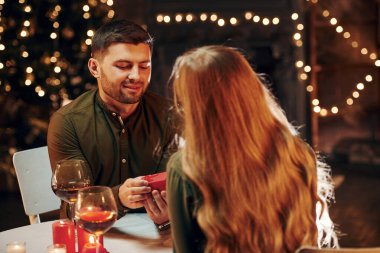Masanın yanında oturuyor. Genç ve güzel çift evde romantik bir akşam yemeği yiyor..