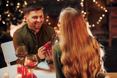 Masanın yanında oturuyor. Genç ve güzel çift evde romantik bir akşam yemeği yiyor..