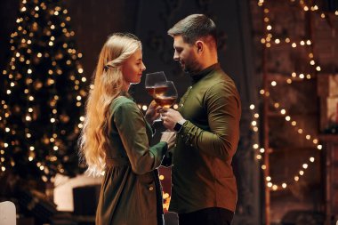 Ayakta ve elinde şarapla büyük bardaklarla. Genç ve güzel çift evde romantik bir akşam yemeği yiyor..