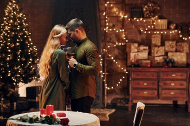 Ayakta ve elinde şarapla büyük bardaklarla. Genç ve güzel çift evde romantik bir akşam yemeği yiyor..