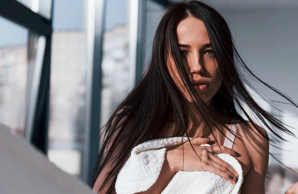 Genç, güzel esmer kız, içeride duruyor ve vücudunu beyaz havluyla örtüyor..