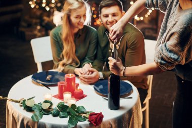 Garson şarap açar. Genç ve güzel çift evde romantik bir akşam yemeği yiyor..