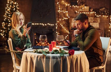 Oturuyor ve telefon kullanıyor. Genç ve güzel çift evde romantik bir akşam yemeği yiyor..