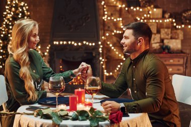 Ellerinden tutarak. Genç ve güzel çift evde romantik bir akşam yemeği yiyor..