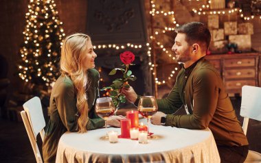 Güzel kırmızı bir gül tutuyordu. Genç ve güzel çift evde romantik bir akşam yemeği yiyor..