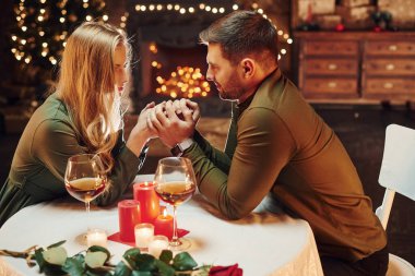 Ellerinden tutarak. Genç ve güzel çift evde romantik bir akşam yemeği yiyor..