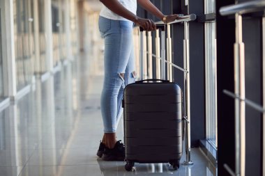 Genç Afro-Amerikan kadın yolcunun parçacık görüntüsü havaalanında bagajlı günlük giysiler içinde..