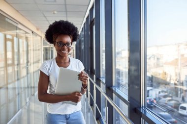 Young african american female passanger in casual clothes is in airport holding laptop.