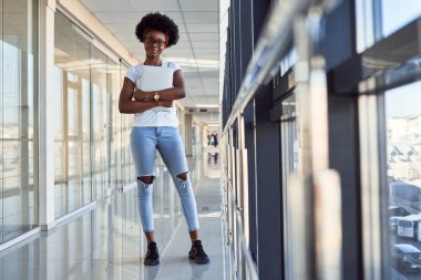 Gündelik giysiler içinde genç Afrikalı Amerikalı kadın yolcu havaalanında elinde dizüstü bilgisayarla bekliyor..