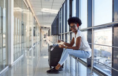 Gündelik giysiler içinde genç Afro-Amerikan bayan yolcu havaalanında bagaj yiyor..