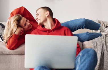 Bacaklarındaki dizüstü bilgisayarı kullanarak. Genç ve sevimli çift hafta sonunu ve tatilleri birlikte geçiriyorlar..