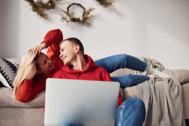 Bacaklarındaki dizüstü bilgisayarı kullanarak. Genç ve sevimli çift hafta sonunu ve tatilleri birlikte geçiriyorlar..