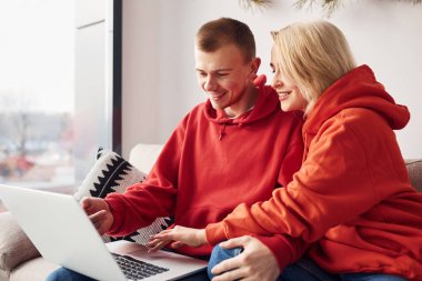 Bacaklarındaki dizüstü bilgisayarı kullanarak. Genç ve sevimli çift hafta sonunu ve tatilleri birlikte geçiriyorlar..