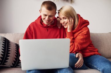 Bacaklarındaki dizüstü bilgisayarı kullanarak. Genç ve sevimli çift hafta sonunu ve tatilleri birlikte geçiriyorlar..