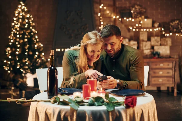 坐下来用电话年轻貌美的夫妻在室内共进浪漫晚餐 — 图库照片