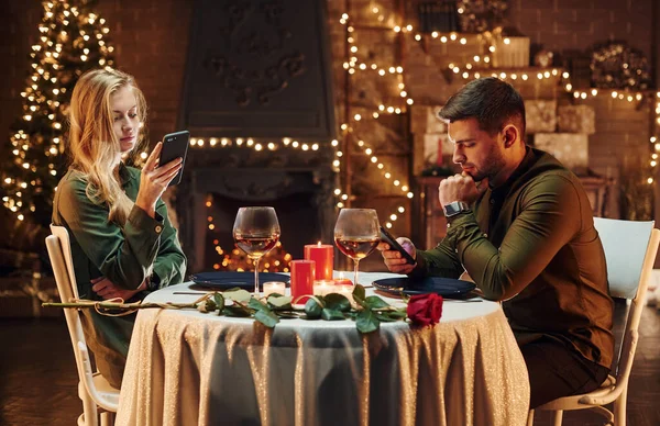 Oturuyor ve telefon kullanıyor. Genç ve güzel çift evde romantik bir akşam yemeği yiyor..