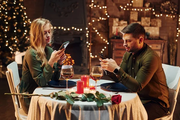 Oturuyor ve telefon kullanıyor. Genç ve güzel çift evde romantik bir akşam yemeği yiyor..