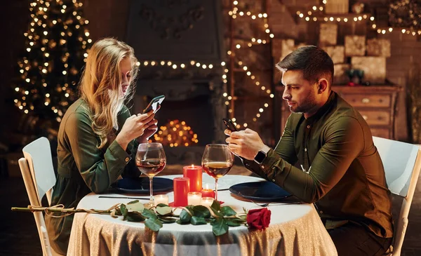 坐下来用电话年轻貌美的夫妻在室内共进浪漫晚餐 — 图库照片