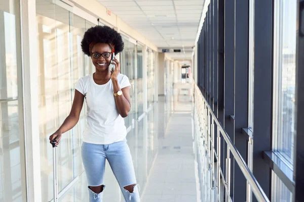 Gündelik giysiler içindeki genç Afrikalı Amerikalı bayan yolcu havaalanında telefonuyla bekliyor..