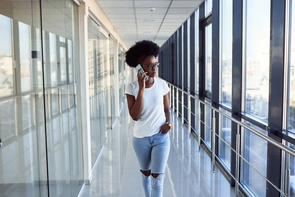 Gündelik giysiler içindeki genç Afrikalı Amerikalı bayan yolcu havaalanında telefonuyla bekliyor..