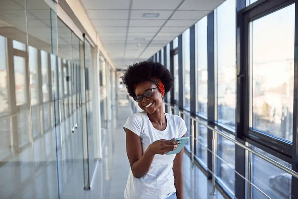 Gündelik giysiler içindeki genç Afrikalı Amerikalı bayan yolcu havaalanında telefonuyla bekliyor..