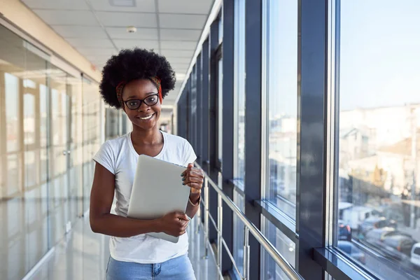Gündelik giysiler içinde genç Afrikalı Amerikalı kadın yolcu havaalanında elinde dizüstü bilgisayarla bekliyor..