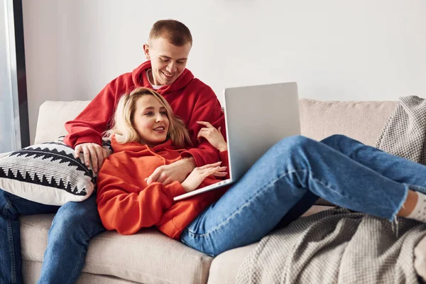 Bacaklarındaki dizüstü bilgisayarı kullanarak. Genç ve sevimli çift hafta sonunu ve tatilleri birlikte geçiriyorlar..