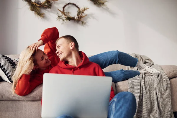 Bacaklarındaki dizüstü bilgisayarı kullanarak. Genç ve sevimli çift hafta sonunu ve tatilleri birlikte geçiriyorlar..