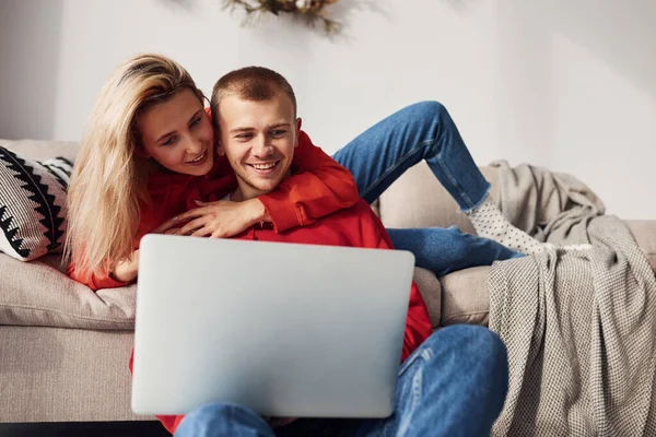 Bacaklarındaki dizüstü bilgisayarı kullanarak. Genç ve sevimli çift hafta sonunu ve tatilleri birlikte geçiriyorlar..