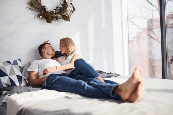 Young lovely couple lying down on bed together at home spending weekend and holidays together.